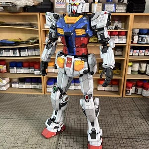 May include: A detailed model of a Gundam robot, featuring a color scheme of white, blue, red, and yellow. The model has intricate panel lines and markings, with the text "EFSF" and "09" visible. The robot is standing upright, showcasing its articulated design.
