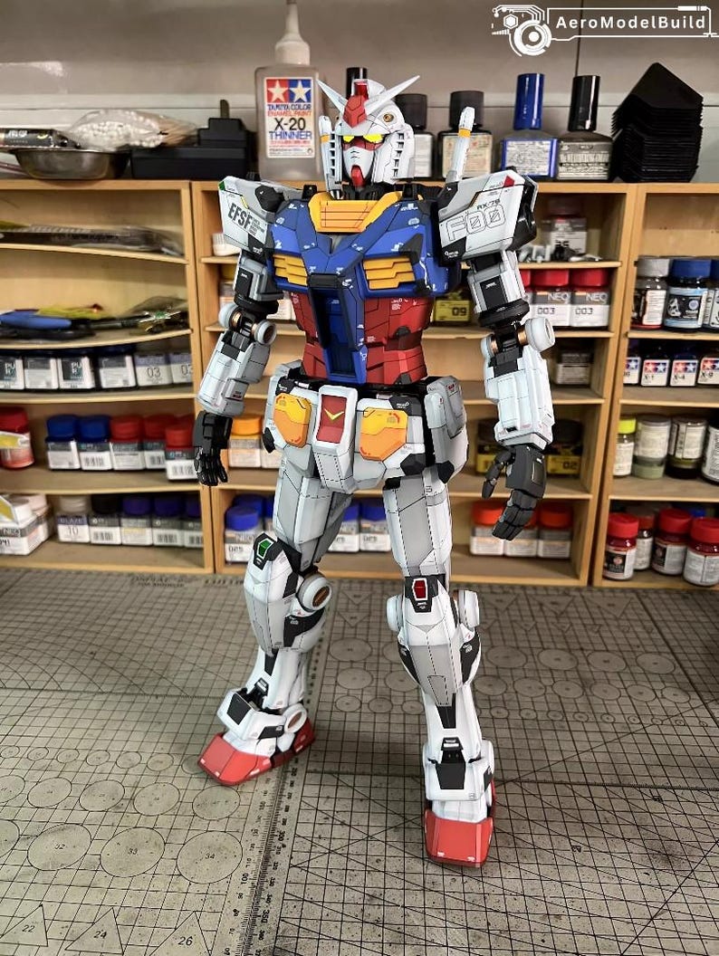 May include: A detailed model of a Gundam robot, featuring a color scheme of white, blue, red, and yellow. The model has intricate panel lines and markings, with the text "EFSF" and "09" visible. The robot is standing upright, showcasing its articulated design.