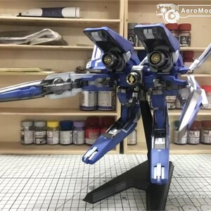 May include: A detailed model of a blue and white aircraft with articulated wings and a black stand. The model has intricate mechanical details and is set against a backdrop of shelves with paint supplies.