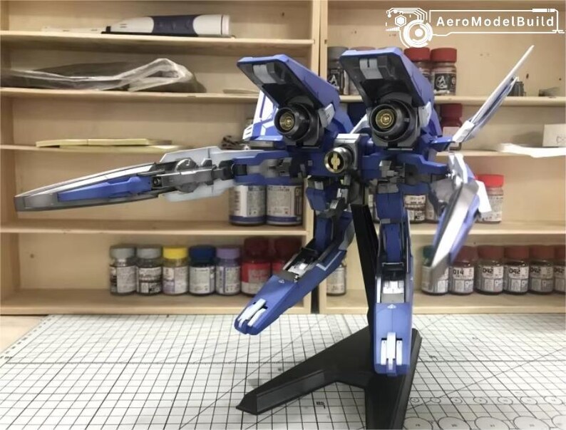 May include: A detailed model of a blue and white aircraft with articulated wings and a black stand. The model has intricate mechanical details and is set against a backdrop of shelves with paint supplies.