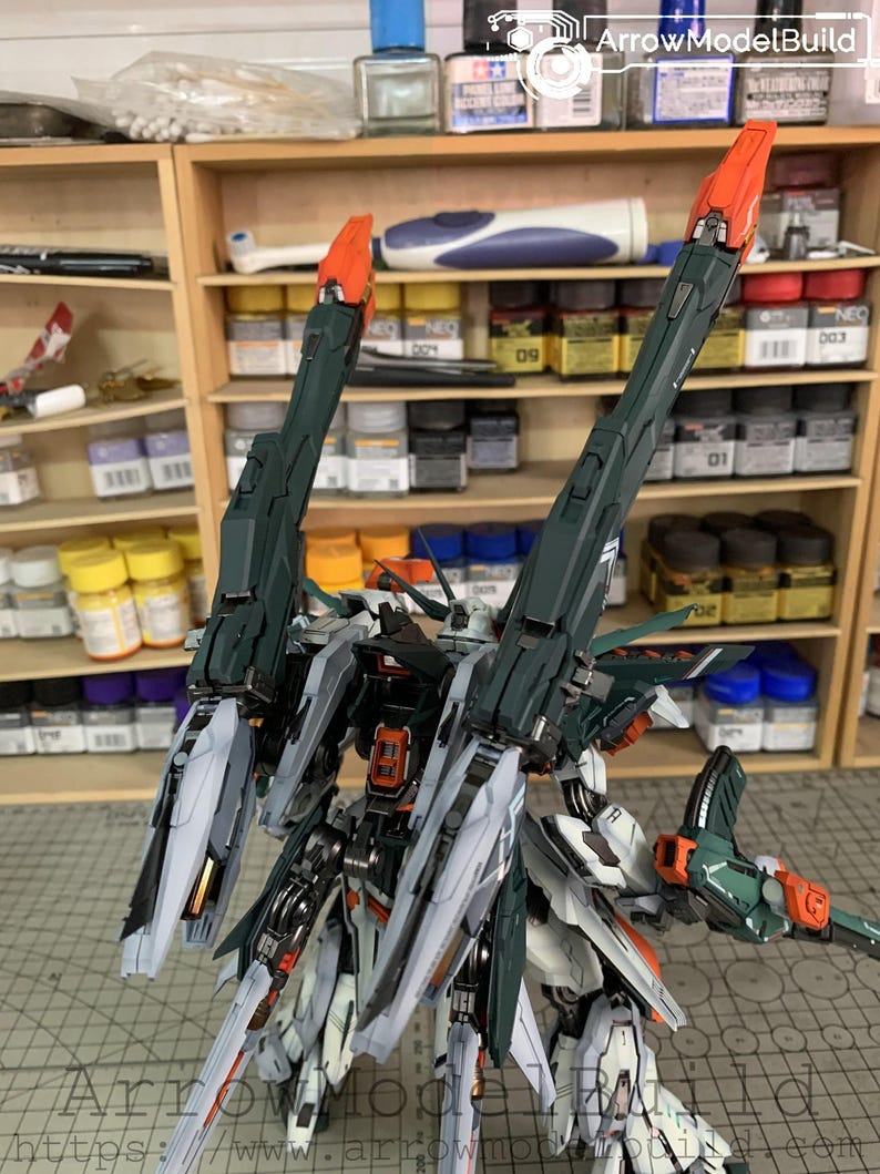 May include: A detailed model kit of a mech robot, featuring a complex design with green, white, and orange accents. The robot has large, angular wings and intricate mechanical details. The background includes shelves with paint supplies and tools.