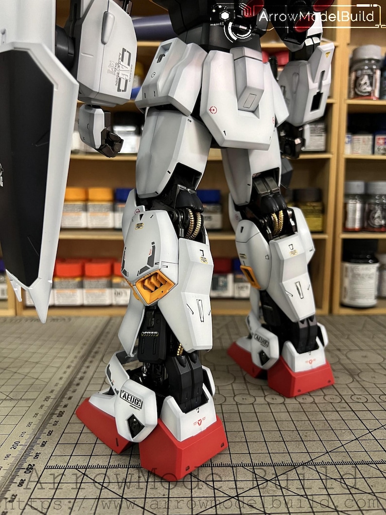 May include: A detailed model of a white and gray robot with red accents on the feet. The robot has intricate mechanical details, including visible joints and panels. The model is partially assembled, showcasing its internal structure. The text "AEUG" is visible on the robot's leg.
