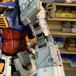 K&ouml;nnte beinhalten: Nahaufnahme eines detaillierten Modellroboters mit wei&szlig;em, rotem, blauem und goldenem Farbschema. Der Roboterarm weist komplizierte mechanische Details auf, einschlie&szlig;lich Tafeln mit Text und roten Akzenten. Das Modell ist teilweise montiert.