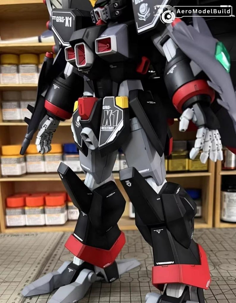 May include: A detailed model of a mecha robot, primarily black, gray, and red. The model features intricate paneling, articulated limbs, and the text "GFAS-K1" and "DESTROY". The robot has a shield and is set against a background of paint supplies.