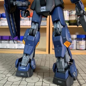 May include: A detailed, partially assembled model kit of a robot, primarily in shades of blue and gray. The model features intricate mechanical details, including segmented legs, with the number "03" visible. The word "TITANS" is printed on the foot.