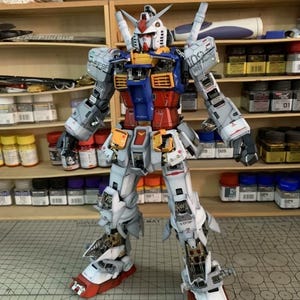 K&ouml;nnte beinhalten: Ein detailliertes Modell eines Gundam-Roboters mit einem Farbschema aus Wei&szlig;, Blau, Rot und Gelb. Das Modell steht aufrecht und zeigt komplizierte mechanische Details und Paneellinien. Der Roboter hat einen markanten Kopf mit rotem Kamm und mehreren Antennen.