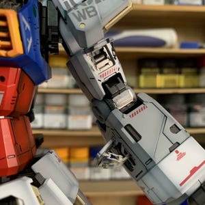 K&ouml;nnte beinhalten: Nahaufnahme eines detaillierten Modellroboterarms. Haupts&auml;chlich grau mit roten und wei&szlig;en Akzenten, mit den Texten "WB" und "EFSF". Das teilweise montierte Modell zeigt komplizierte mechanische Details.