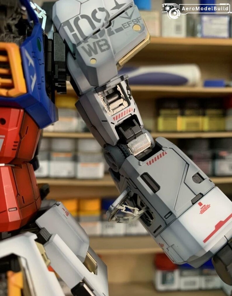 K&ouml;nnte beinhalten: Nahaufnahme eines detaillierten Modellroboterarms. Haupts&auml;chlich grau mit roten und wei&szlig;en Akzenten, mit den Texten "WB" und "EFSF". Das teilweise montierte Modell zeigt komplizierte mechanische Details.