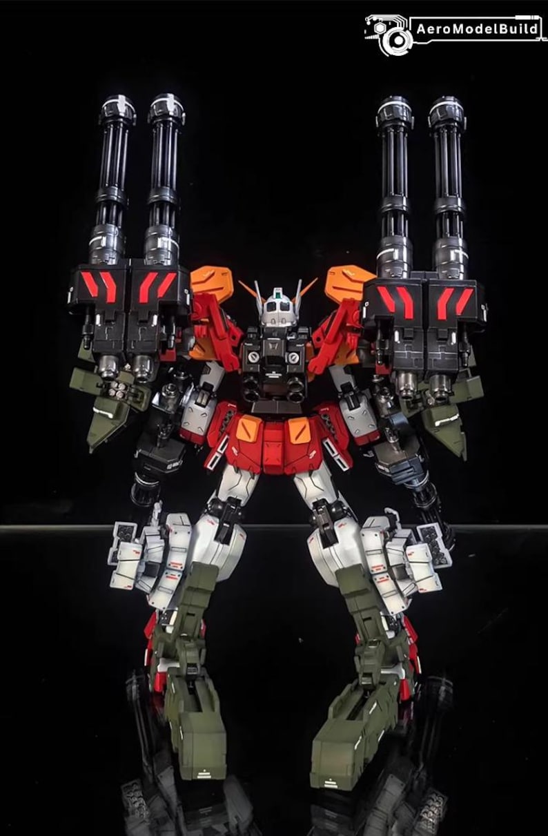 May include: A detailed model robot in red, white, black, and green. The robot has multiple cannons and weapons attached to its shoulders and back. The AeroModelBuild logo is in the top right corner.