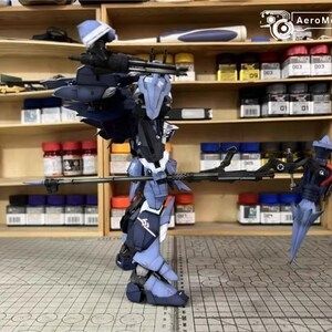 May include: A detailed model of a futuristic robot, primarily in shades of blue and black, with intricate mechanical details. The robot is posed with a long weapon, and the background shows shelves with paint bottles and model-building supplies.