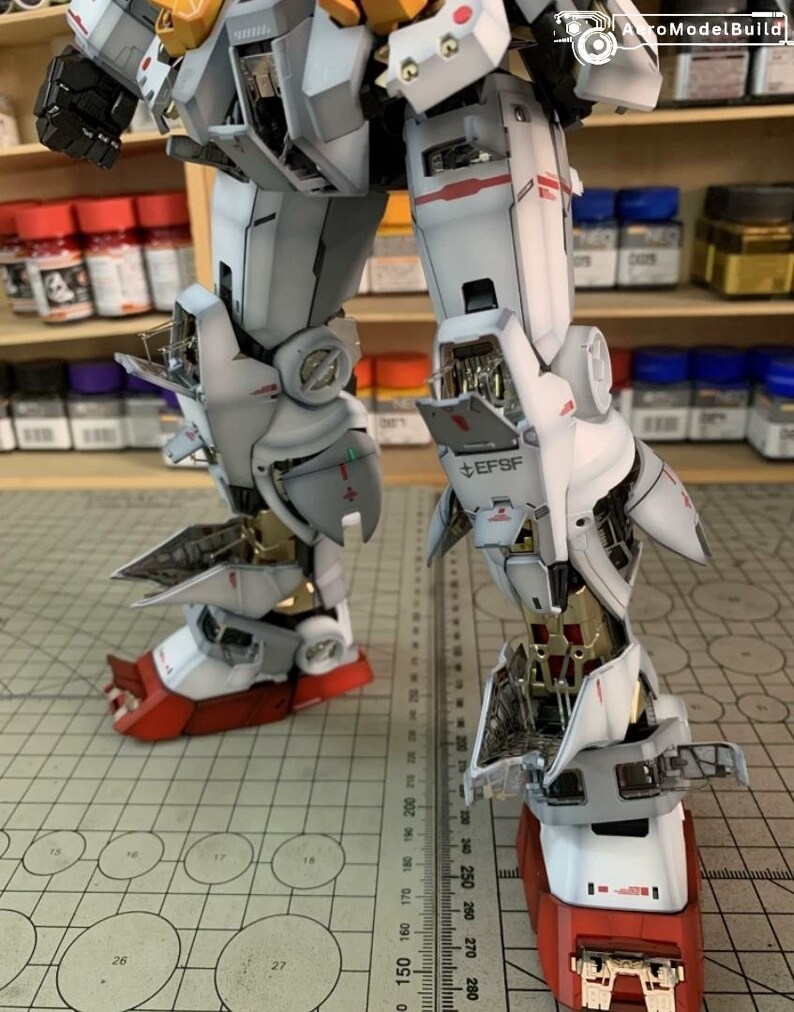 K&ouml;nnte beinhalten: Nahaufnahme der Beine eines Modellroboters, die komplexe mechanische Details zeigen. Die Beine sind &uuml;berwiegend wei&szlig; mit roten und goldenen Akzenten. Der Text "EFSF" ist sichtbar. Das Modell befindet sich auf einer Schneidematte.
