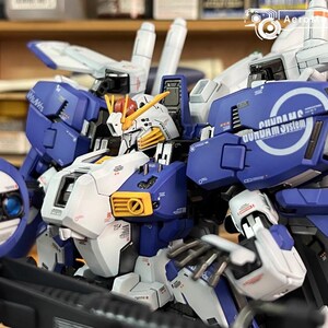 May include: A detailed model of a Gundam robot, mainly blue, white, and yellow. The model has intricate mechanical details, including panels, vents, and articulated joints. The text "GUNDAM system" is visible on the shoulder. A collectible item.