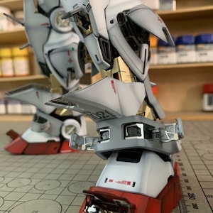 K&ouml;nnte beinhalten: Nahaufnahme eines detaillierten Modellroboterbeins. Das Bein ist &uuml;berwiegend wei&szlig; mit roten und goldenen Akzenten. Das Modell weist komplizierte mechanische Details auf, einschlie&szlig;lich sichtbarer interner Komponenten und dem Text "EFSF".