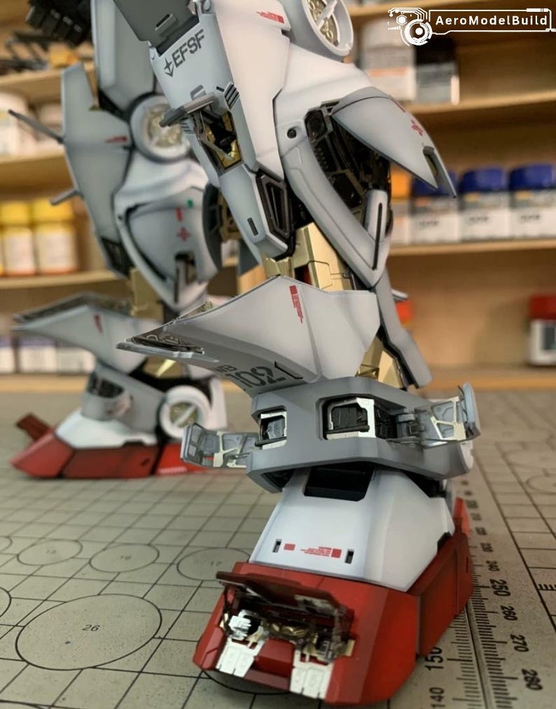 K&ouml;nnte beinhalten: Nahaufnahme eines detaillierten Modellroboterbeins. Das Bein ist &uuml;berwiegend wei&szlig; mit roten und goldenen Akzenten. Das Modell weist komplizierte mechanische Details auf, einschlie&szlig;lich sichtbarer interner Komponenten und dem Text "EFSF".