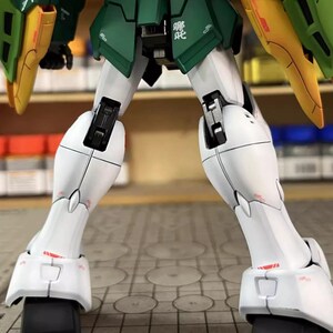 May include: A detailed model robot kit, predominantly white, green, and yellow. The image focuses on the legs and feet, highlighting intricate mechanical details. The model has black accents. The text "ArrowModelBuild" is visible in the image.