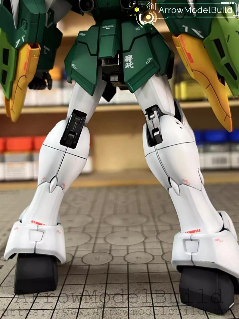 May include: A detailed model robot kit, predominantly white, green, and yellow. The image focuses on the legs and feet, highlighting intricate mechanical details. The model has black accents. The text "ArrowModelBuild" is visible in the image.