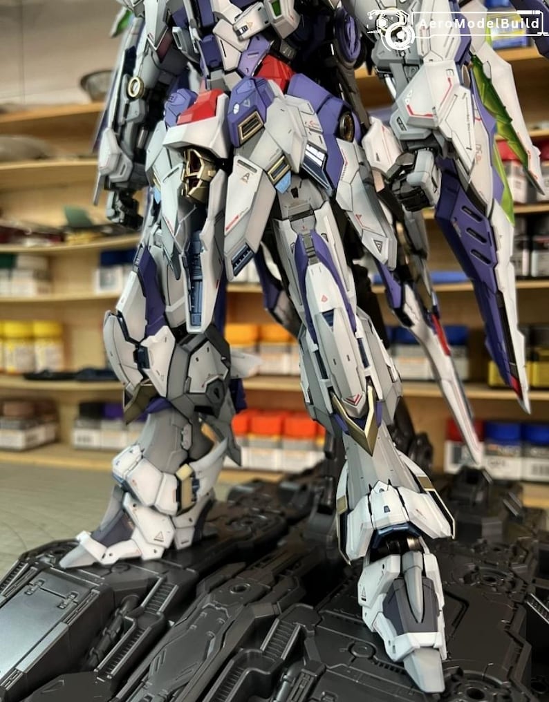 May include: A highly detailed robot model, predominantly white, grey, purple and red. The model is posed on a black surface, highlighting its intricate mechanical design. The model's design includes sharp angles and complex paneling.