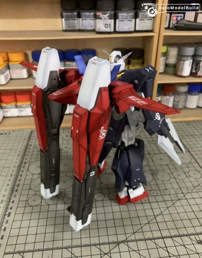 Puede incluir: Un modelo detallado de un robot mec&aacute;nico, con una combinaci&oacute;n de colores rojo, blanco, negro y azul. El modelo tiene grandes piezas de armadura angulares y alas. El modelo est&aacute; sobre una esterilla de corte con una regla.