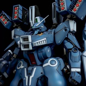 May include: A detailed, blue model robot with multiple missile launchers and white accents. The robot has a complex design with various panels, vents, and a head with a white antenna. The AeroModelBuild logo is in the top right corner.