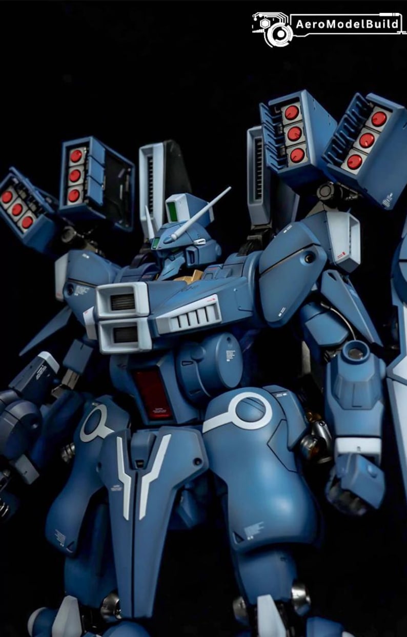 May include: A detailed, blue model robot with multiple missile launchers and white accents. The robot has a complex design with various panels, vents, and a head with a white antenna. The AeroModelBuild logo is in the top right corner.