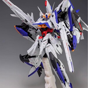 Puede incluir: Maqueta detallada de un robot futurista, predominantemente blanco con detalles azules, rojos y negros. El robot presenta un intrincado blindaje, grandes alas y una cabeza estilizada. Est&aacute; montado sobre un soporte blanco.