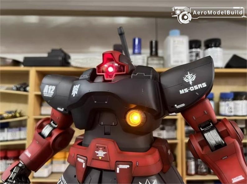 May include: A detailed model of a black and red robot with illuminated red and yellow lights. The robot has the text "A12" and "MS-OSRS" on its body. The AeroModelBuild logo is visible in the top right corner.