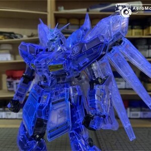 May include: A detailed, translucent blue model robot, featuring articulated limbs and wing-like elements. The robot is displayed in a dynamic pose, highlighting its intricate design. Shelves with containers are in the background, indicating a hobby or model-making setting. The text "AeroModelBuild" is visible.