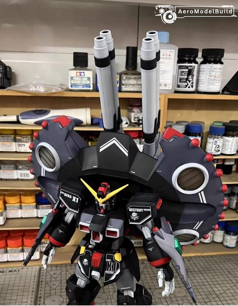 May include: A detailed model of a black, gray, and red mecha robot with large shoulder armor and multiple missile launchers. The model has yellow and red accents, with the text "GFFS-X1" and "DESTROY" visible. The model is on a shelf with various model-building supplies.