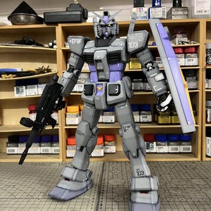 May include: A detailed model of a gray and purple robot with a gun and shield. The robot has the text "EFSF" and "WB 103" on its body. The model is standing on a surface with a ruler and the text "ArrowModelBuild".