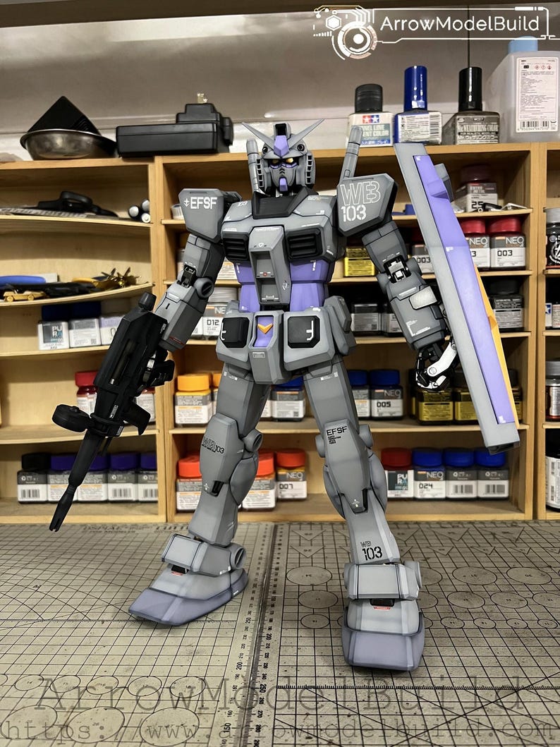 May include: A detailed model of a gray and purple robot with a gun and shield. The robot has the text "EFSF" and "WB 103" on its body. The model is standing on a surface with a ruler and the text "ArrowModelBuild".