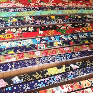 May include: A collection of colorful Japanese origami paper strips. The strips feature various floral and geometric patterns in red, blue, gold, and white. The paper is arranged in parallel rows, showcasing the diverse designs.
