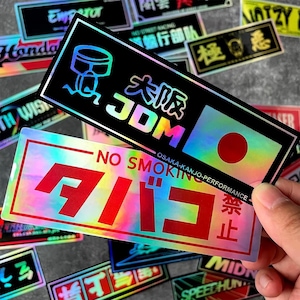 Könnte beinhalten: Holografische Aufkleber mit japanischem Text und Grafiken. Ein Aufkleber zeigt "JDM" und ein japanisches Flaggen-Design. Der andere Aufkleber hat rote japanische Schriftzeichen und die Worte "NO SMOKING".