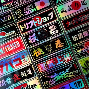 May include: A collection of holographic stickers with Japanese text and graphics. The stickers feature various designs, including kanji characters, logos, and phrases. Colors include black, red, and iridescent hues.