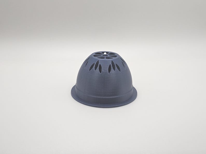 Op de afbeelding: Een donkergrijs, klokvormig object met een uitlopende basis en decoratieve uitsparingen. De bovenkant van het object heeft een reeks bloemblad-vormige openingen. Het object lijkt te zijn gemaakt van een vast materiaal, mogelijk plastic of keramiek.