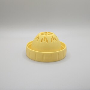 Op de afbeelding: Een geel, 3D-geprint keukengadget, waarschijnlijk een zeef of vergiet. Het ontwerp heeft een gewelfde bovenkant met decoratieve uitsparingen en een brede, geribbelde basis. Het object is gemaakt van massief, matgeel plastic.