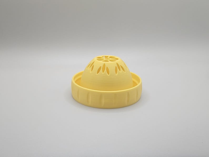 Op de afbeelding: Een geel, 3D-geprint keukengadget, waarschijnlijk een zeef of vergiet. Het ontwerp heeft een gewelfde bovenkant met decoratieve uitsparingen en een brede, geribbelde basis. Het object is gemaakt van massief, matgeel plastic.