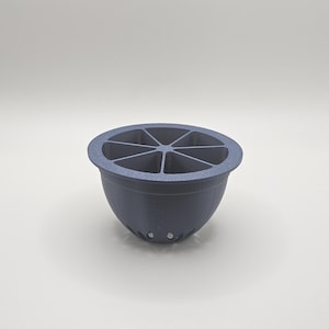 Op de afbeelding: Een donkerblauw, komvormig object met een gesegmenteerd interieur, dat lijkt op een citrusvrucht. De kom heeft een afgeronde basis en een reeks kleine gaatjes aan de onderkant. De bovenkant is verdeeld in zes secties.