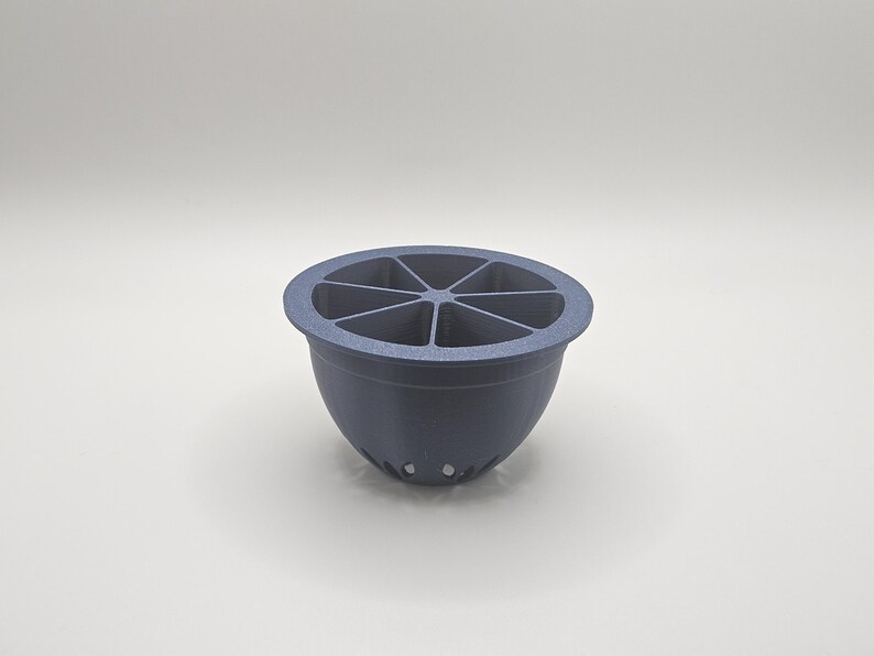Op de afbeelding: Een donkerblauw, komvormig object met een gesegmenteerd interieur, dat lijkt op een citrusvrucht. De kom heeft een afgeronde basis en een reeks kleine gaatjes aan de onderkant. De bovenkant is verdeeld in zes secties.
