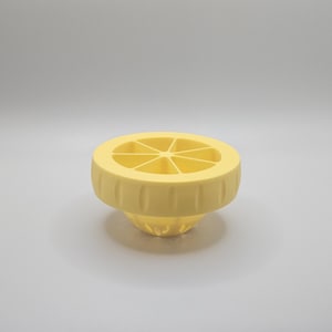 Op de afbeelding: Een gele citruspers met een gesegmenteerde bovenkant en een geribbelde basis. Deze pers is gemaakt van plastic en is ontworpen om sap uit citroenen en andere citrusvruchten te persen. Het ontwerp is eenvoudig en functioneel.