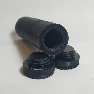 May include: Black cylindrical object with a threaded interior, plus two smaller, matching black caps. The caps have a circular design with a threaded exterior. The items are on a white surface.