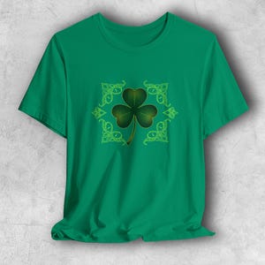 Könnte beinhalten: Ein grünes T-Shirt mit einem Kleeblatt-Design. Das Kleeblatt ist ein dreiblättriges Kleeblatt mit Farbverlauf, umgeben von einem keltischen Knotenmuster. Das T-Shirt hat eine einfarbige grüne Farbe.