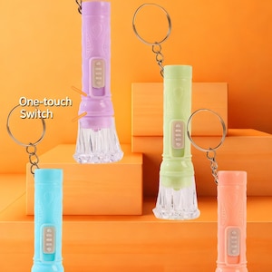 Puede incluir: Mini linternas en morado, verde, azul y naranja, cada una con un llavero. Las linternas tienen una base transparente y texturizada y un botón. El texto de la imagen dice "Mini flashlight", "One-touch Switch", "Evening Illumination", "Portable Design" y "Uneven Lens Surface".