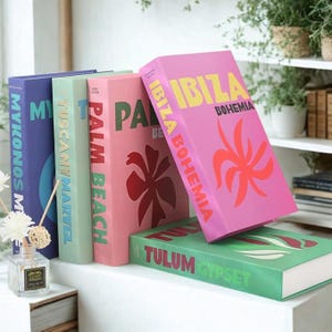 May include: A selection of colourful decorative books. The books are in shades of blue, green, pink, and green. The titles include "Mykonos," "Tuscany," "Palm Beach," "Ibiza Bohemia," and "Tulum." Each book has a unique design and font.
