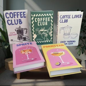 Op de afbeelding: Een verzameling decoratieve boeken met koffie- en cocktailthema's. De boeken tonen illustraties van koffiezetapparaten, kopjes en cocktails. De tekst op de boeken bevat "Coffee Club", "Coffee Lover Club", "Spritz Cocktail" en "Pornstar Martini".