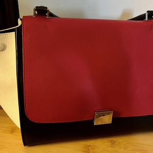 May include: A red, black, and white leather handbag with a flap closure and a gold-toned clasp.