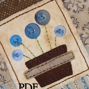 Pode incluir: Um padrão PDF para uma parede acolchoada com um vaso marrom com botões azuis e brancos costurados como flores. O texto "PDF PATTERN" está impresso abaixo da imagem.