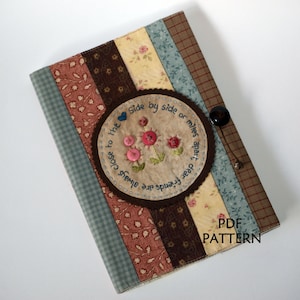 May include: A handmade fabric journal cover with a brown circle applique featuring the text "Side by side or miles apart, dear friends are always close to the" and a floral design with pink and blue buttons. The cover is made with a variety of patterned fabrics in shades of brown, blue, pink, and yellow. The text "PDF PATTERN" is printed in white on the bottom right corner of the cover.