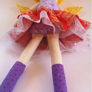 May include: A handmade doll with yellow hair, a purple and orange dress, and purple polka dot socks. The doll is wearing a tulle skirt and has wings.