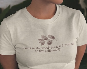 May include: A white t-shirt with a brown leafy branch design and the text "I went to the woods because I wished to live deliberately."