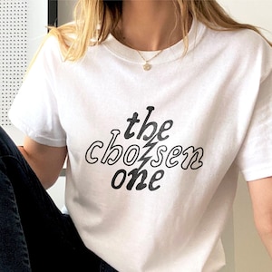 May include: A white t-shirt with black text that reads "the chosen one" in a stylized font.
